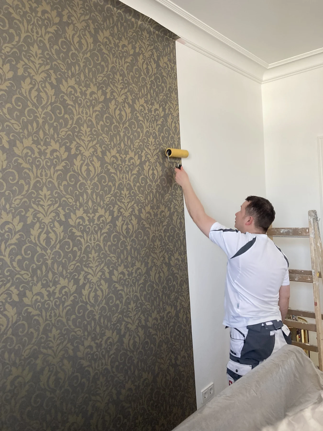 Handwerker bei Tapezierarbeiten an einer Wand mit ornamentaler Tapete