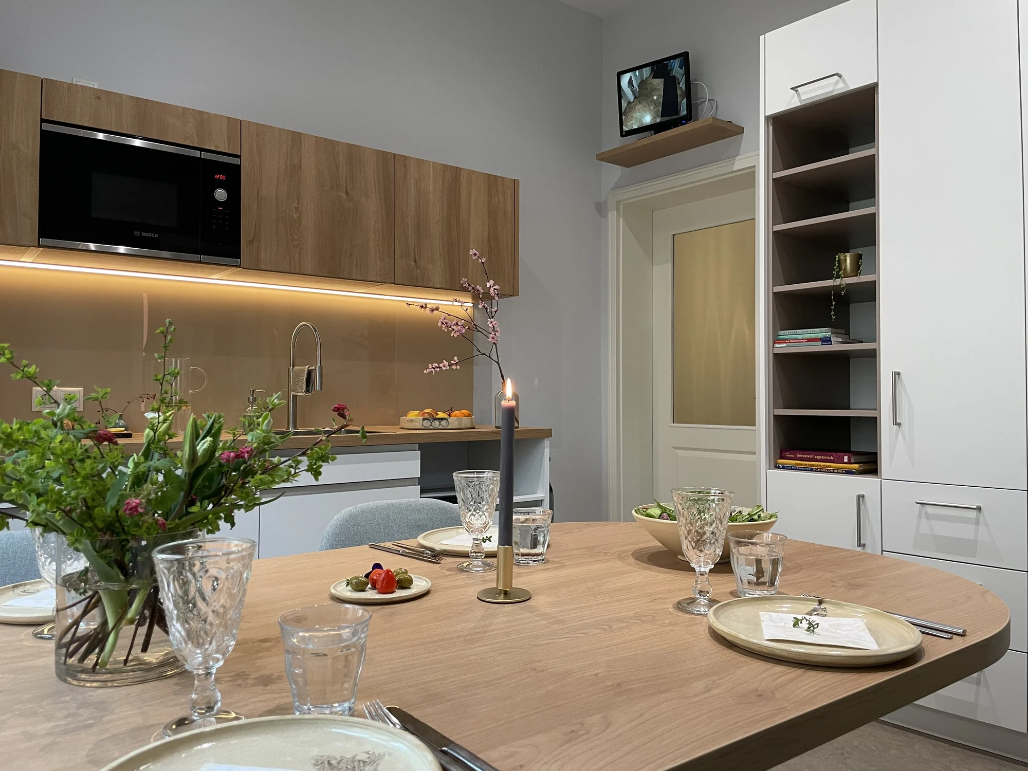 Küche mit Holzfronten, indirekter Beleuchtung und gedecktem Esstisch mit Blumen